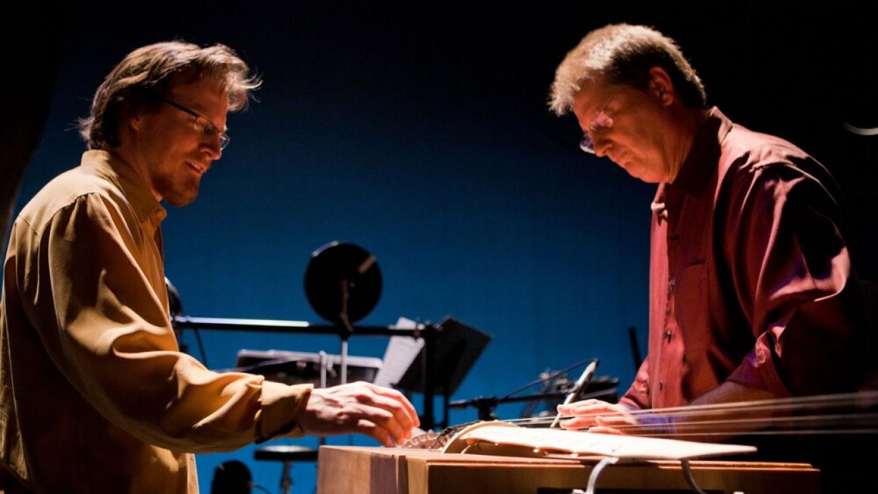 Musicians Paul Dresher and Joel Davel face each other while playing one of their invented instruments in performance.